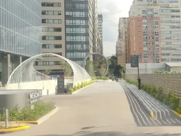 The Eye of Mexico sculpture frames an urban pathway between modern high-rise buildings and landscaped greenery.