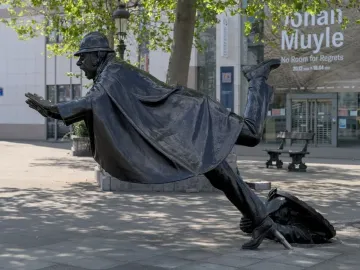 Vaartkapoen sculpture showing a bronze man in a helmet being pulled backward into a hole in the pavement.