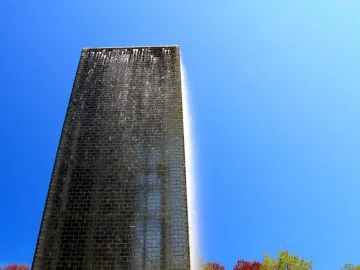 Crown Fountain tower with water cascading down its dark brick-like surface against a blue sky.