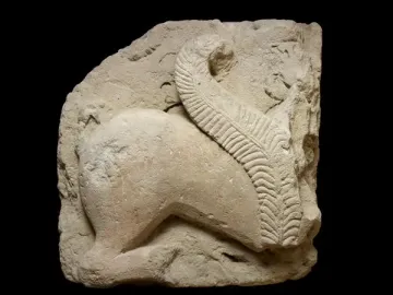 Weathered stone fragment of the El Salobral Sphinxes showing the hindquarters and curved body of an animal with a textured tail arched over its back.