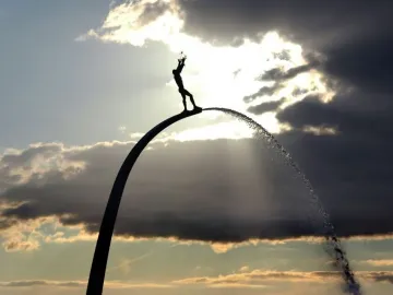 Silhouetted figure atop the God, Our Father on the Rainbow fountain with water cascading down the arch.