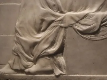 Close-up of Madonna of the Stair showing the lower half of the relief, with draped fabric, bare feet, and stair-like lines in the background.