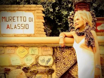 Decorated stone wall of the Muretto di Alassio with a sign at the top and ceramic tiles covered in signatures and sketches.
