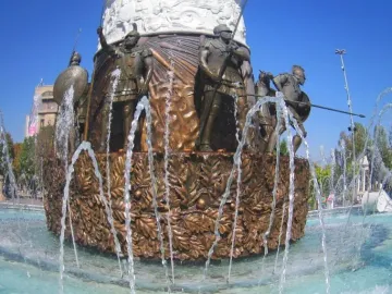 Bronze base of the Warrior on Horseback monument with armored warriors, spears, shields, and surrounding fountain jets.