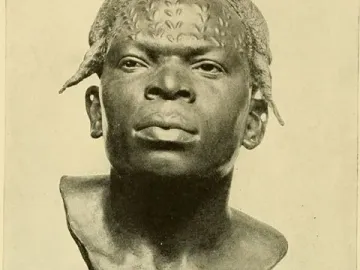 Dark bust of an Aruwimi Native with raised patterns on the forehead and scalp, mounted on a simple pedestal.