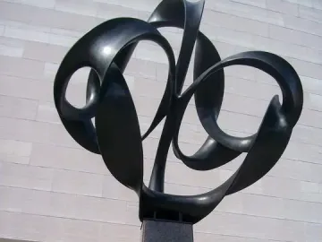 Continuum, a tall abstract metal sculpture with looping ribbons on a granite pedestal outside a modern building.
