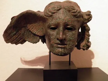 Bronze head of Hypnos with a wing on the side, shown on a black stand.
