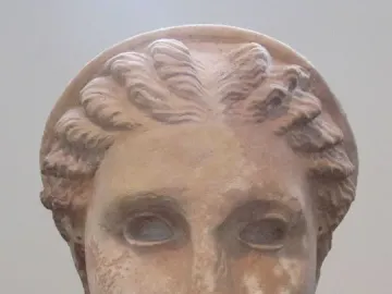 Weathered stone head of Lycosoura Artemis on a pedestal, with braided hair and a wreath.