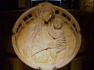 Madonna del Perdono relief showing a haloed mother holding a child, with cherubs in the background and a decorative border.