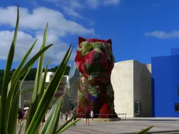 Puppy floral dog sculpture covered in red, pink, white, and green flowers in an outdoor plaza.