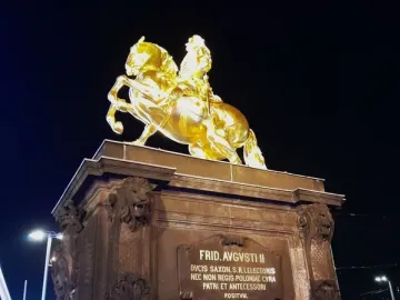 The Golden Rider equestrian statue glows against the night sky on a tall stone pedestal.