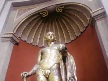 Gilded Hercules statue holding a club and wearing a lion skin, set in a decorative niche.