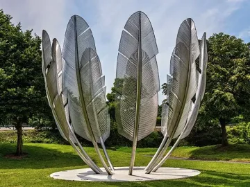 Kindred Spirits sculpture with tall silvery feather-like forms arranged in a circle on a grassy lawn.