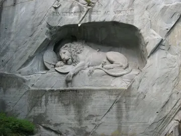 The Lion Monument in Luzern showing a wounded lion carved into a rock grotto with a shield and broken spear.