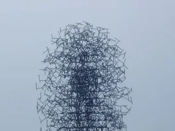 Quantum Cloud sculpture of thin dark metal rods forming a large oval shape beside the water.