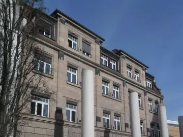 Tall white pillars of the Way of Human Rights stand in front of a stone building with many windows.