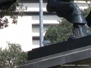 Close-up of a dark sculpture detail at Plaça de Catalunya with a pigeon perched on the ledge below a carved leg and hoof.