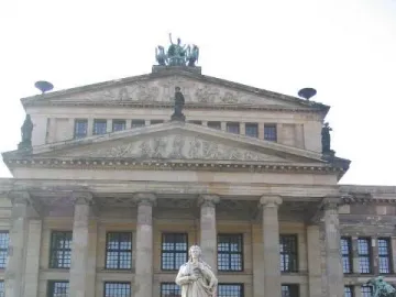 Schiller Monument with seated allegorical figures at its base in front of a classical building.