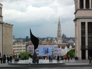 The Whirling Ear sculpture in a circular fountain in a public plaza, with a city spire in the background.