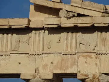 Fragmentary Parthenon pediment stonework with carved horse figures against a blue sky.