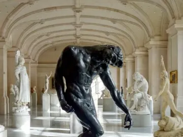 The Shade, a dark muscular nude male sculpture with a hunched posture and bowed head in a museum hall.