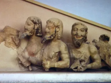 Trisomatos Typhon carved in light-colored stone with three bearded heads and traces of original pigment.