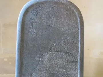 Mesha Stele, a tall dark stone slab covered in ancient carved script with missing fragments and visible cracks.