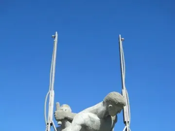 Sztafeta sculpture showing two nude male figures against a blue sky, with metal supports around the figures.
