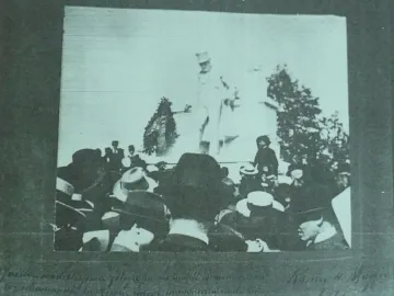Crowd gathered around the Monument to Giuseppe Gioachino Belli, with a tall statue of a man in a top hat at the center.
