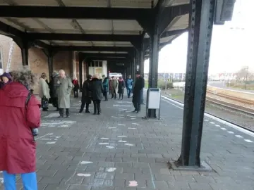 People gathered on a train station platform near the Kindertransport monument, with a large pink and blue chalk Union Jack drawn on the ground.
