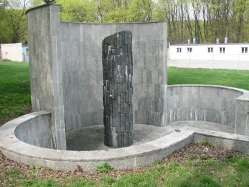 Monument of Common Martyrdom, a tall dark pillar of irregular blocks within a curved stone enclosure.