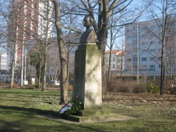 Richard Wagner bust on a moss-covered stone pedestal in a grassy park setting.