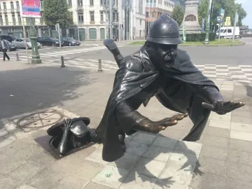 Vaartkapoen bronze sculpture showing a uniformed policeman falling as a figure emerges from an open manhole and grabs the cover.