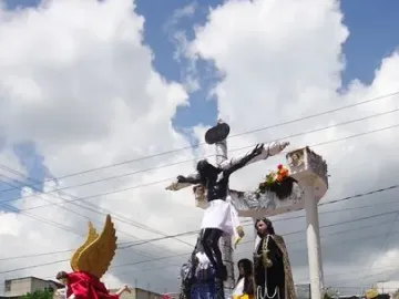 A religious procession carries an ornate float with the San Juan Patrón sculpture and a crucifix, surrounded by flowers and costumed participants.