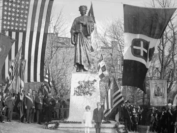 Dante Alighieri statue on a granite pedestal, surrounded by flags and a crowd at a dedication ceremony.