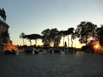 Monument to Giuseppe Garibaldi lit by warm light above a cobbled plaza, with parked cars and silhouetted trees at sunset.