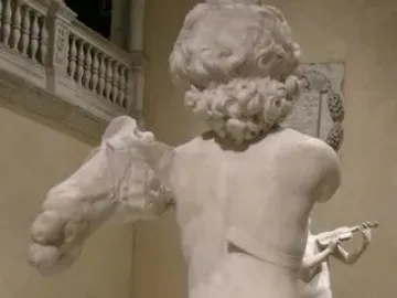 Back view of the fragmented Young Archer marble sculpture, showing a nude curly-haired male figure with missing arms and lower legs.