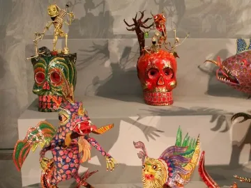 Colorful alebrije sculptures with hybrid creature features and decorated skulls on tiered platforms.
