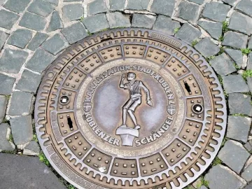 Circular manhole cover featuring the Schängel boy figure and the text \