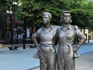 Women of Steel sculpture showing two female figures standing arm in arm on a paved walkway.