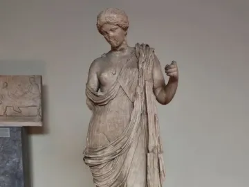 Armed Aphrodite marble statue on a pedestal in a museum gallery.
