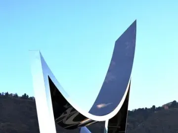 Life Electric sculpture with reflective silver panels against blue sky and distant hills.