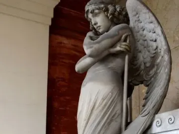 Monteverde Angel, a winged stone angel with bowed head and crossed arms holding a long staff, standing on a tiered base.