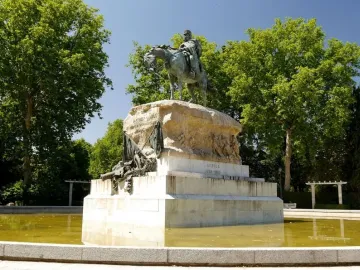 Monument to General Martínez-Campos with an equestrian bronze statue on a tiered stone pedestal in a pool surrounded by trees.