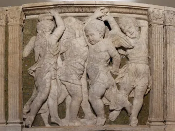 Marble relief from the Pulpit of Prato Cathedral showing dancing figures and winged putti against a dark mosaic background.