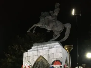 The Statue of Honor illuminated at night, with wreaths and placards arranged around its pedestal.