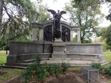 Titanic Engineers\' Memorial with a winged female figure above bronze relief panels in a park setting.