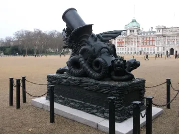 The Cádiz Memorial stands on Horseguards Parade, with an ornate dark sculptural base and a cannon-like barrel rising upward in front of a large classical building.