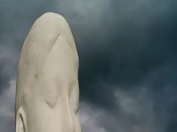 The Dream sculpture, a pale segmented head and neck with closed eyes, stands against dark cloudy skies.