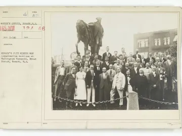 A large group of men and one woman pose in tiers in front of the George Washington monument.